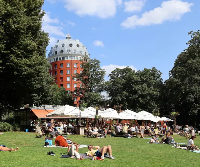 Mensen op het gras in Park Valkenberg, met boven de bomen het torengebouw Poort van Breda