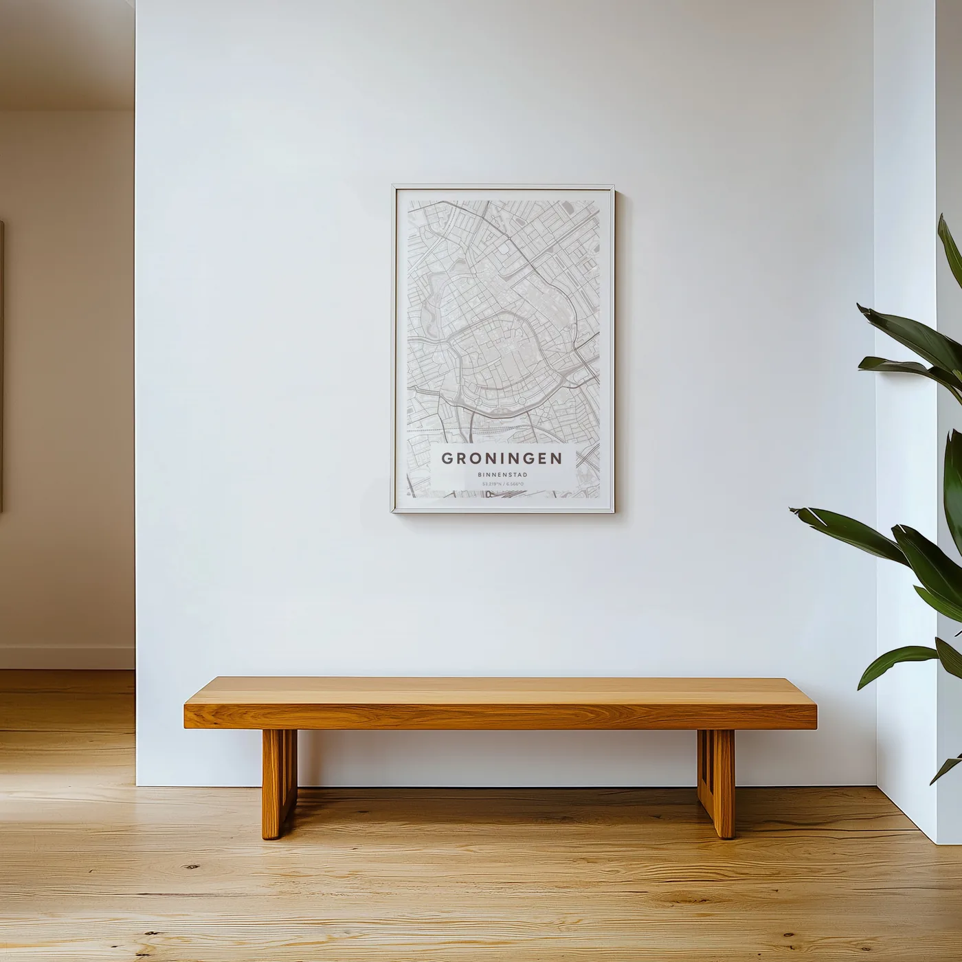 De poster van Groningen in Mauve in een lichte lijst aan een witte muur, boven een lange houten bank